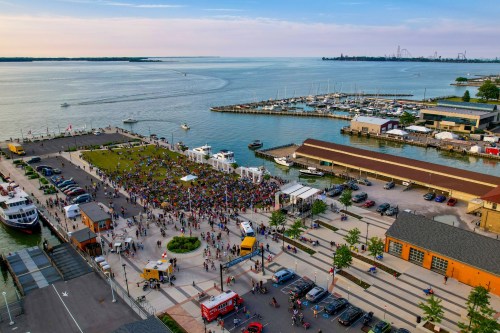 Aerial view of a crowded waterfront area with boats, a marina, and a festival taking place along the shore.