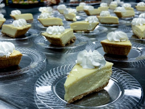 A close-up of mini cheesecake slices topped with whipped cream, arranged on clear plastic plates.