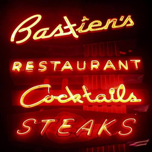 Neon sign for Bastien's Restaurant featuring "Cocktails" and "Steaks" in bright red letters.