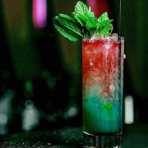 A colorful layered cocktail with mint leaves, served in a tall glass with a straw.