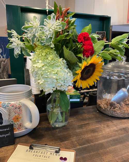 A vibrant bouquet of flowers, including sunflowers and hydrangeas, sits on a counter next to a breakfast menu.