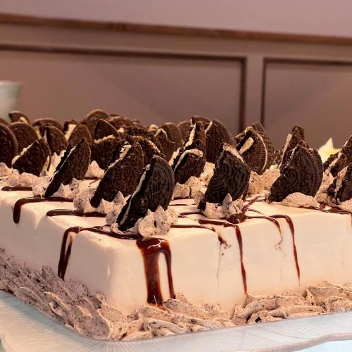 A rectangular cake topped with whipped cream, chocolate drizzle, and Oreo cookie halves.