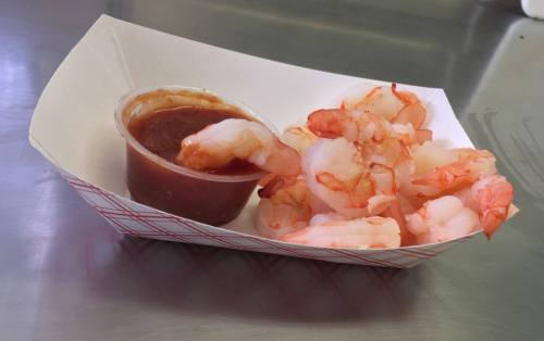 A serving of shrimp with a small cup of cocktail sauce in a paper tray.