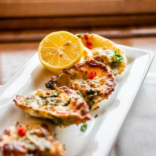 A plate of baked seafood dishes garnished with herbs and a lemon wedge, served on a white platter.