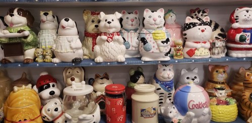 A colorful display of various ceramic cat and dog figurines and cookie jars on a shelf.
