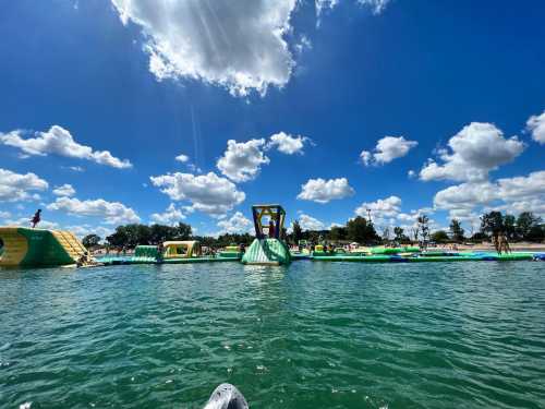 A sunny day at a water park with inflatable structures and people enjoying the water under a blue sky with fluffy clouds.