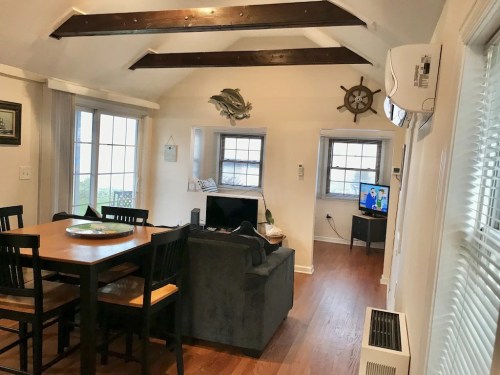 Cozy living area with a dining table, sofa, and TV, featuring wooden beams and nautical decor.