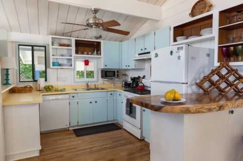 Bright kitchen with light blue cabinets, white appliances, and wooden accents, featuring a fruit bowl on the counter.