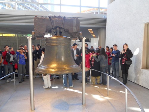 A large bell on display with a crowd of people taking photos in a modern indoor space.