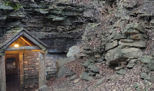A small stone entrance set into a rocky hillside, surrounded by dry leaves and natural stone formations.