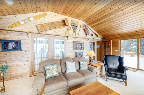 Cozy wooden living room with a sofa, armchair, and rustic decor, featuring snowshoes and a view of the outdoors.