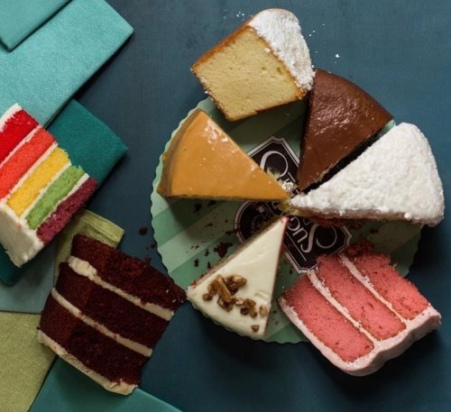 A colorful assortment of cake slices on a teal background, including red velvet, rainbow, and chocolate cakes.