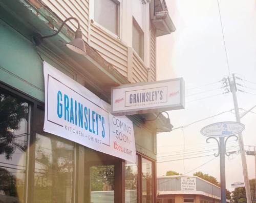 Signage for Grainsley's Kitchen & Drinks, with a "Coming Soon" banner, located in a commercial area.