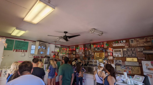 A busy ice cream shop with a crowd of customers, colorful decorations, and a variety of signs on the walls.