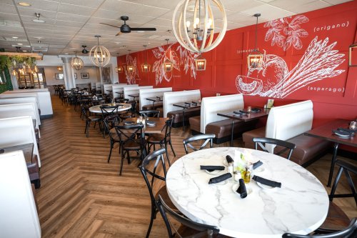 Modern restaurant interior with red walls, white booths, round marble tables, and stylish light fixtures.