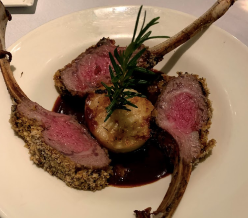 A plate featuring rack of lamb with a herb crust, served with a round potato and garnished with rosemary.