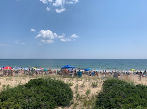 A crowded beach scene with colorful umbrellas, people enjoying the sun, and a clear blue sky over the ocean.