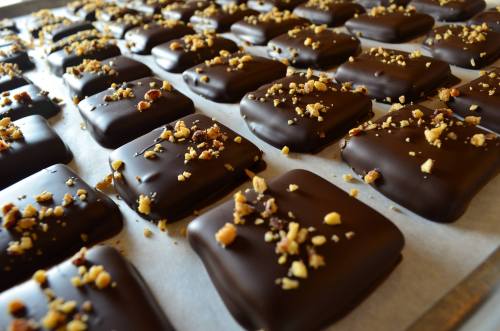 A close-up of chocolate-covered treats topped with crushed nuts, arranged neatly on a baking sheet.