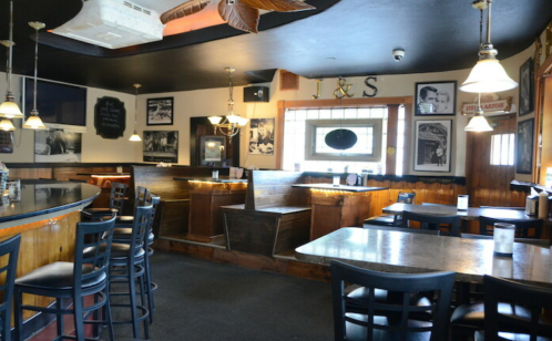Interior of a cozy bar with wooden seating, dim lighting, and vintage decor on the walls.