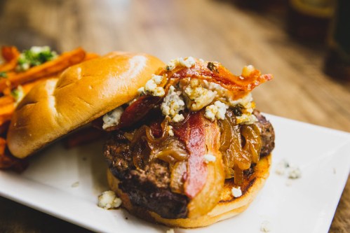 A juicy burger topped with bacon, caramelized onions, and blue cheese, served with sweet potato fries on the side.