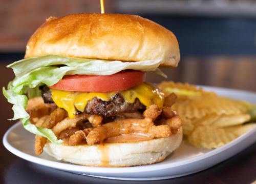 A juicy cheeseburger with lettuce, tomato, and crispy fries, served on a toasted bun with a side of potato chips.