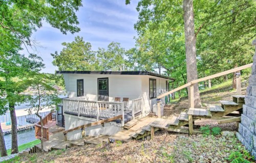 A modern white house with a deck, surrounded by trees, and a wooden staircase leading down to a lake.