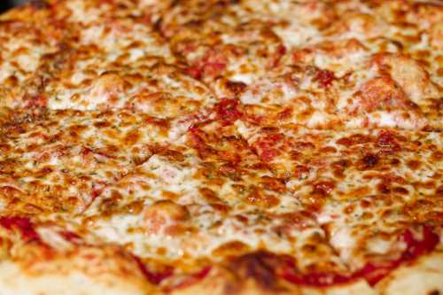 Close-up of a cheesy pizza with golden-brown crust and melted cheese, sliced into triangular pieces.