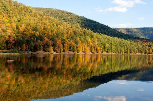 A serene lake reflecting vibrant autumn foliage and rolling hills under a clear blue sky.