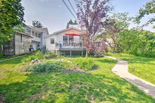 A cozy house with a deck and an umbrella, surrounded by greenery and a pathway in a sunny backyard.