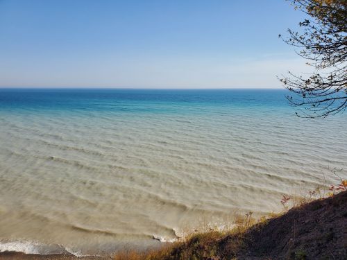 A serene view of a calm lake with gentle waves, framed by a clear blue sky and a hint of shoreline vegetation.