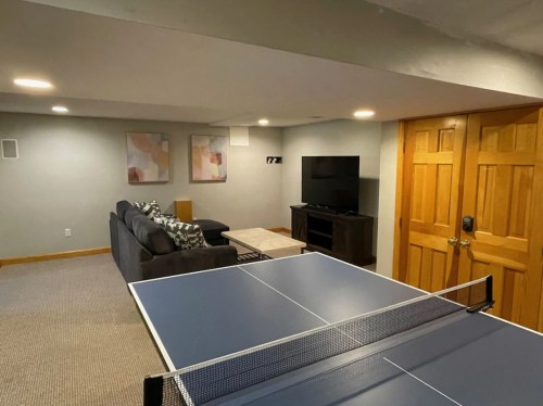 A cozy basement with a ping pong table, sofa, coffee table, TV, and wall art.