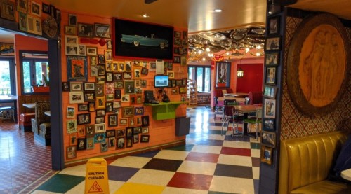 Colorful restaurant interior featuring a wall of framed photos, vibrant decor, and a caution sign on the floor.