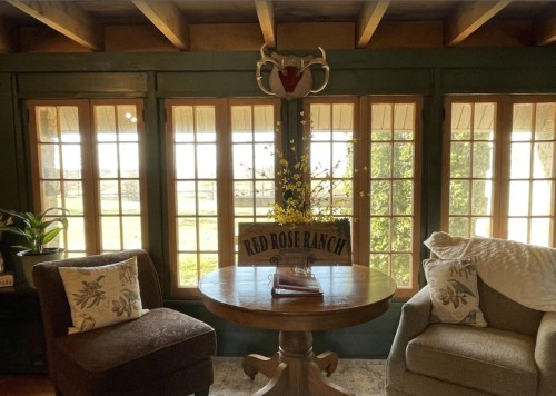 Cozy interior with two armchairs, a round table, and large windows showcasing a scenic view outside.