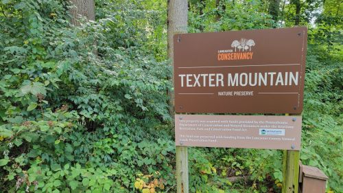 Sign for Texter Mountain Nature Preserve, surrounded by greenery, indicating conservation efforts and funding sources.
