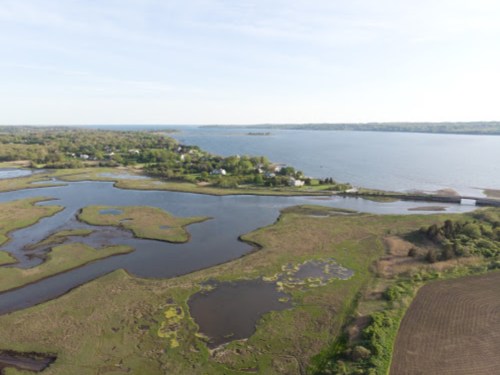 Aerial view of a serene landscape featuring a river, marshland, and lush greenery under a clear sky.