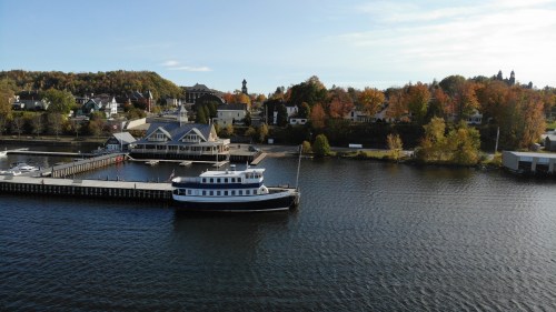 A scenic view of a boat docked by a waterfront, surrounded by autumn-colored trees and charming buildings.