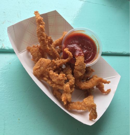 A serving of crispy fried calamari with a small cup of marinara sauce on a paper tray.