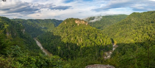 A panoramic view of lush green mountains and a winding river under a partly cloudy sky.
