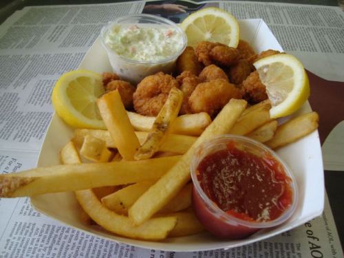A basket of golden fried shrimp, French fries, coleslaw, and lemon wedges, served with a side of dipping sauce.