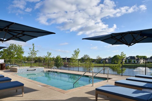 A serene pool area with lounge chairs, umbrellas, and a view of a lake under a clear blue sky.
