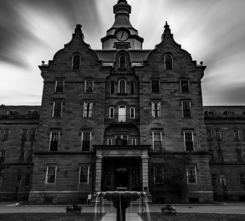 A historic building with a clock tower, featuring a fountain in the foreground, captured in dramatic black and white.