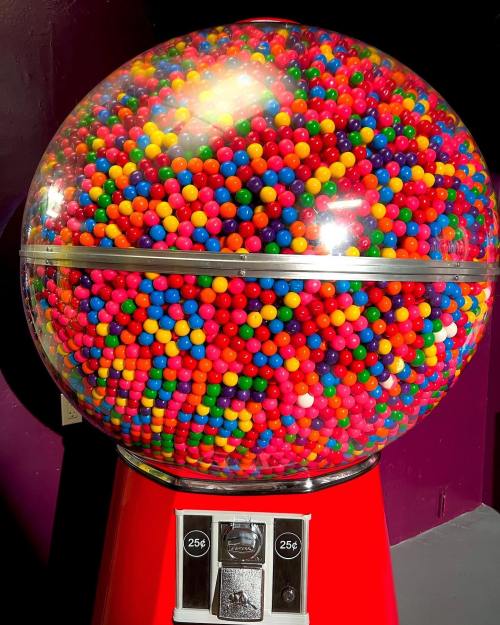 A colorful gumball machine filled with vibrant, multicolored gumballs, set against a purple background.