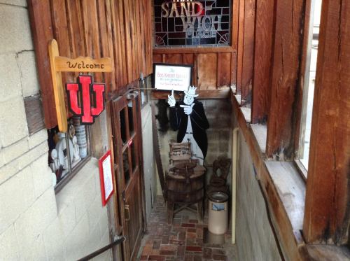 A staircase leading to a rustic entrance with wooden walls, a welcome sign, and a character in a tuxedo.