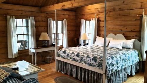 Cozy log cabin bedroom with a four-poster bed, floral bedding, wooden walls, and natural light from windows.