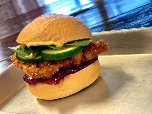 A crispy chicken sandwich with pickles and sauce on a soft bun, served on a metal tray.