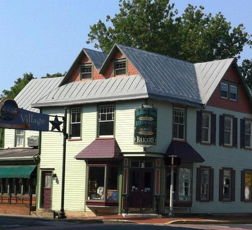 A charming two-story building with a bakery sign, featuring a sloped roof and colorful exterior in a quaint village setting.