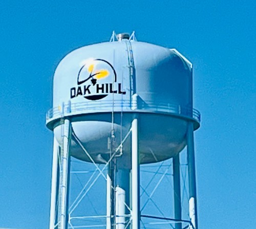 A blue water tower with the text "OAK HILL" and a yellow design against a clear blue sky.