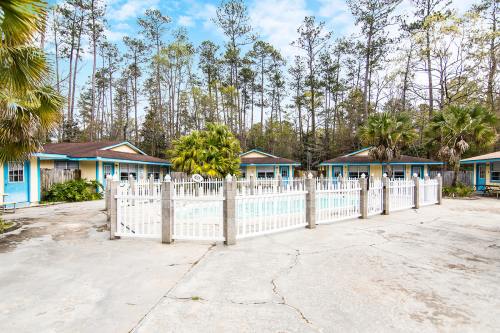 A serene pool area surrounded by cottages and palm trees, set against a backdrop of tall trees and a clear blue sky.