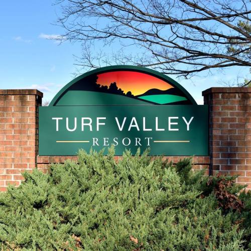 Sign for Turf Valley Resort, featuring a colorful landscape design, surrounded by greenery and a clear blue sky.