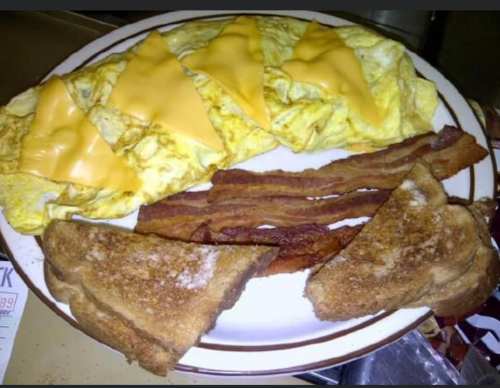 A plate with a cheese omelette, crispy bacon strips, and two slices of toasted bread.